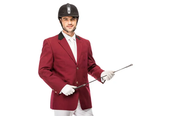 Sonriente jinete joven en uniforme sosteniendo palo de jinete y mirando a la cámara aislada en blanco - foto de stock