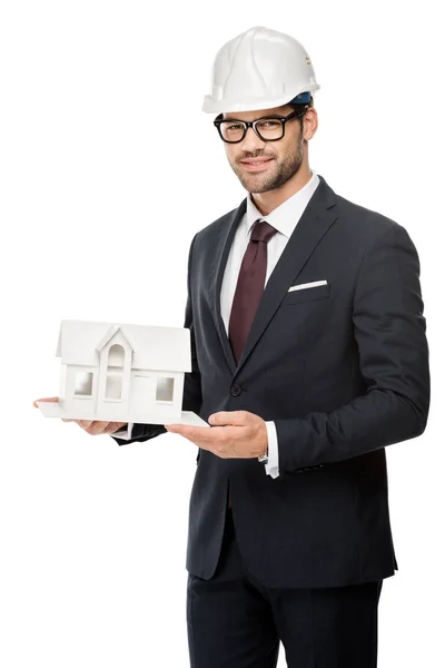 Jeune architecte masculin en casque rigide montrant maison miniature isolée sur blanc — Photo de stock