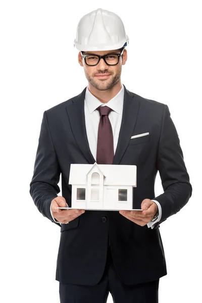 Впевнений молодий чоловік архітектор у жорсткому капелюсі, що показує мініатюрний будинок ізольований на білому — стокове фото