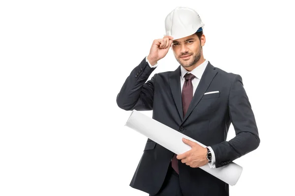 Happy young male architect in suit holding blueprints and adjusting hard hat isolated on white — Stock Photo