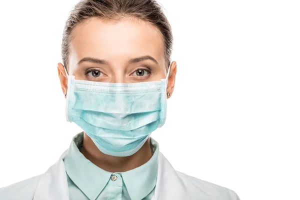 Retrato de la joven doctora en máscara médica mirando a la cámara aislada en blanco - foto de stock