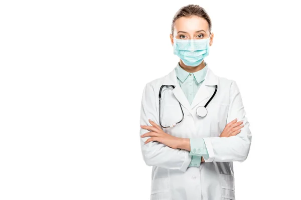 Médico fêmea em máscara médica com estetoscópio sobre o pescoço em pé com braços cruzados isolados em branco — Fotografia de Stock