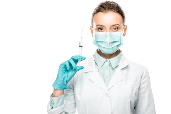 Médico femenino grave con mascarilla médica que sostiene la jeringa aislada en blanco - foto de stock