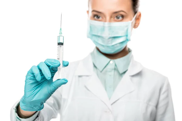 Focused female doctor in medical mask looking at syringe isolated on white — Stock Photo