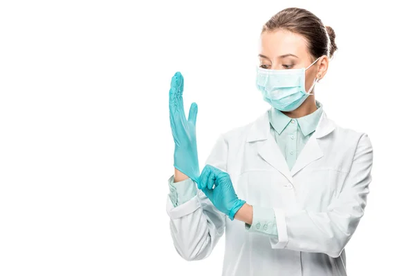 Young female doctor in medical mask putting on latex gloves isolated on white — Stock Photo