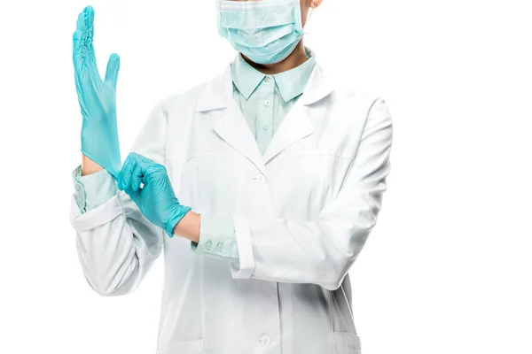 Imagen recortada de la doctora en máscara médica poniéndose guantes de látex aislados en blanco - foto de stock