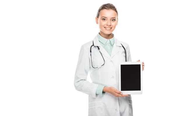 Улыбающаяся женщина врач в медицинском пальто показывает цифровой планшет с чистым экраном изолированы на белом — стоковое фото