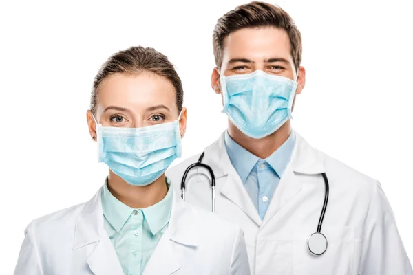 Retrato de jóvenes médicos felices en máscaras médicas mirando a la cámara aislada en blanco - foto de stock