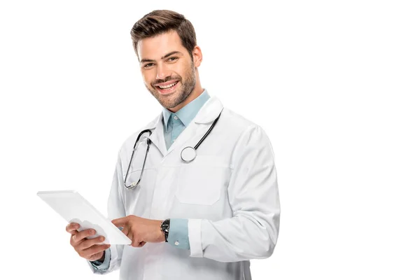 Giovane medico sorridente in cappotto medico utilizzando tablet digitale isolato su bianco — Foto stock