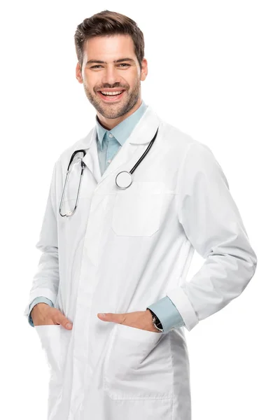 Улыбающийся молодой врач-мужчина со стетоскопом на шее в медицинском халате, изолированном на белом — стоковое фото