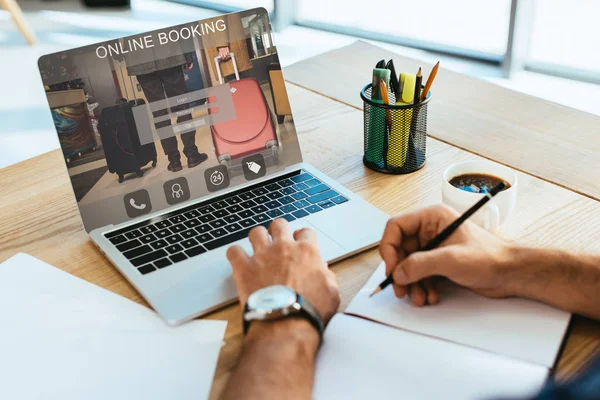 Обрезанный снимок бизнесмена, работающего за столом с ноутбуком и ноутбуком с буквами онлайн-бронирования на экране — стоковое фото