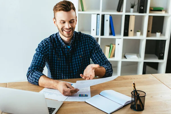 Uomo d'affari sorridente che fa scartoffie da tavolo con computer portatile in ufficio — Foto stock