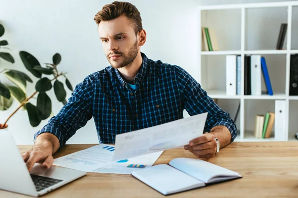 Retrato de empresário focado fazendo papelada na mesa com laptop no escritório — Fotografia de Stock