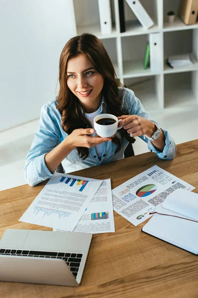 Young businesswoman with cup of coffee at workplace with papers and laptop in office — Stock Photo