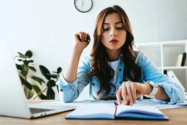 Junge fokussierte Geschäftsfrau am Arbeitsplatz mit Papieren und Laptop im Büro — Stockfoto