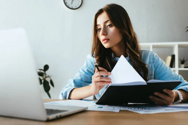 Portrait of young businesswoman with notebook at workplace with papers and laptop in office — Stock Photo