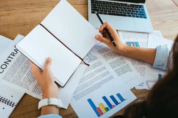 Cropped shot of businesswoman with blank notebook at workplace with papers and laptop in office — Stock Photo