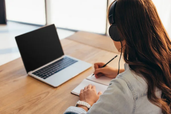 Teilbild einer Geschäftsfrau mit Kopfhörer und Notebook, die an einem Webinar im Büro teilnimmt — Stockfoto