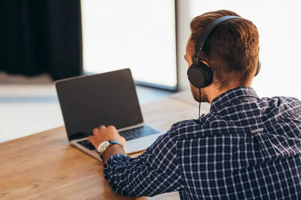 Partial view of man in headphones taking part in webinar at tabletop with notebook in office — Stock Photo