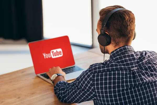 Partial view of man in headphones using laptop with youtube logo on screen in office — Stock Photo