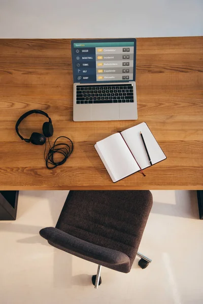 Top view of laptop, headphones and notebook on wooden table with office chair near by — Stock Photo