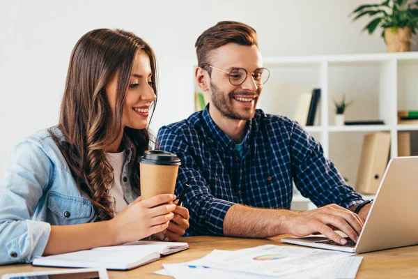 Lächelnde Geschäftskollegen beim Webinar am Tisch mit Papieren und Laptop im Büro — Stockfoto