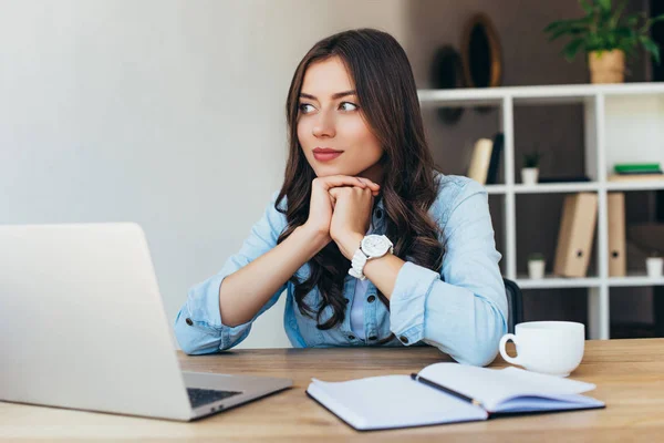 Nachdenkliche Frau am Tisch mit Laptop nimmt an Webinar im Büro teil — Stockfoto