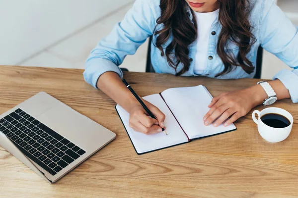 Teilansicht einer Frau, die sich Notizen macht, während sie an einem Webinar im Büro teilnimmt — Stockfoto