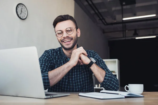 Portrait of cheerful businessman at workplace with laptop and notebook in office — Stock Photo