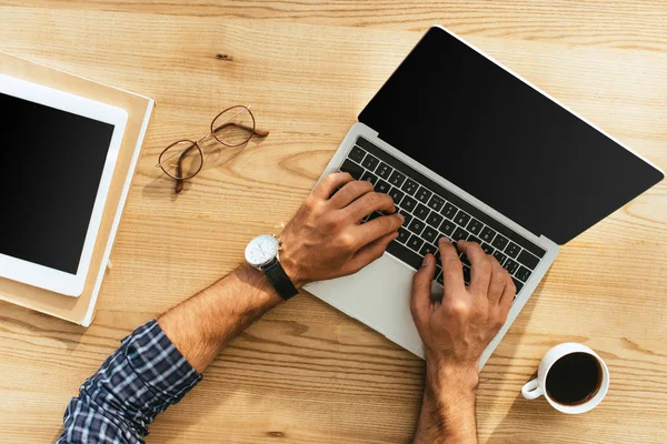 Vista parcial del hombre de negocios que trabaja en el ordenador portátil con pantalla en blanco en la mesa con la tableta y la taza de café - foto de stock