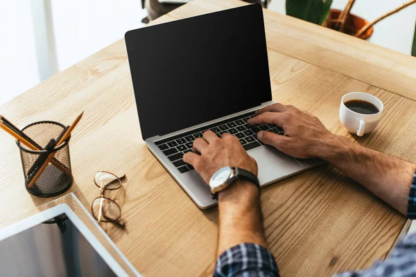 Vue partielle de l'homme d'affaires travaillant sur ordinateur portable avec écran blanc à la table avec tasse de café — Photo de stock