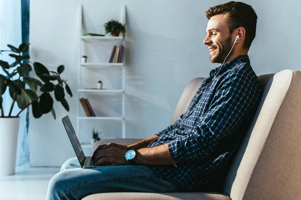 Side view of smiling man in earphones taking part in webinar at home — Stock Photo