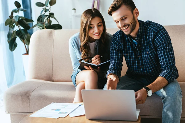 Colegas de negocios sonrientes en la superficie con el ordenador portátil y los papeles que participan en webinar juntos en la oficina - foto de stock