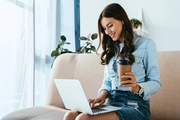 Donna sorridente con caffè per andare sul divano prendendo parte al webinar a casa — Foto stock