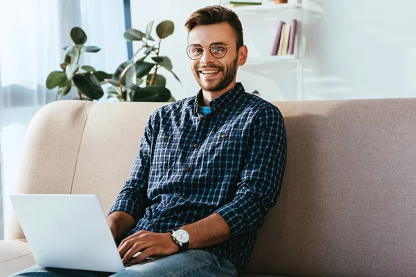 Portrait of smiling man in eyeglasses with laptop sitting on sofa at home — Stock Photo