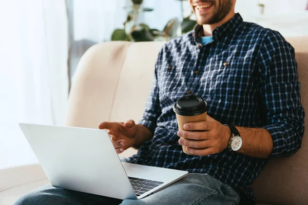 Обрезанный снимок человека с кофе, чтобы пойти и ноутбук принимает участие в вебинаре дома — стоковое фото