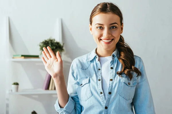 Porträt einer fröhlichen jungen Frau, die zu Hause in die Kamera winkt — Stockfoto