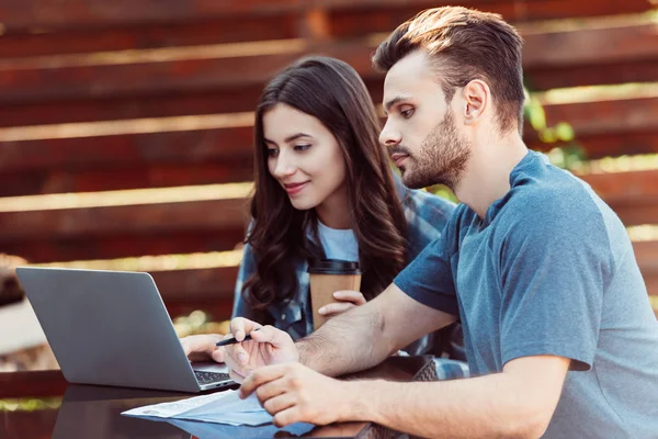 Giovani amici al tavolo con computer portatile e caffè per andare a prendere parte al webinar insieme nel caffè — Foto stock