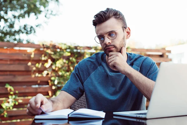 Pensive handsome man taking part in webinar and looking at notebook in park — Stock Photo