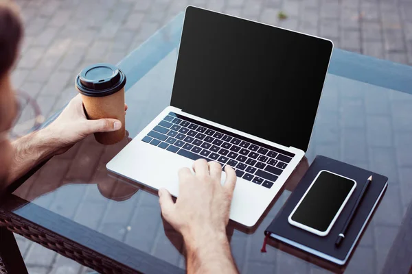 Cropped image of man using laptop with blank screen at table in street cafe — Stock Photo