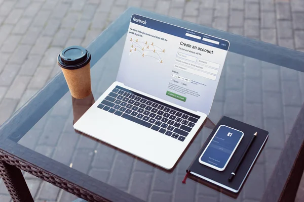 Ordinateur portable et smartphone avec des pages facebook chargées sur la table sur la rue — Photo de stock