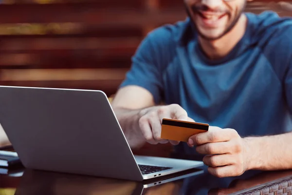 Imagen recortada de hombre de compras en línea con tarjeta de crédito y portátil en la mesa en la cafetería de la calle - foto de stock