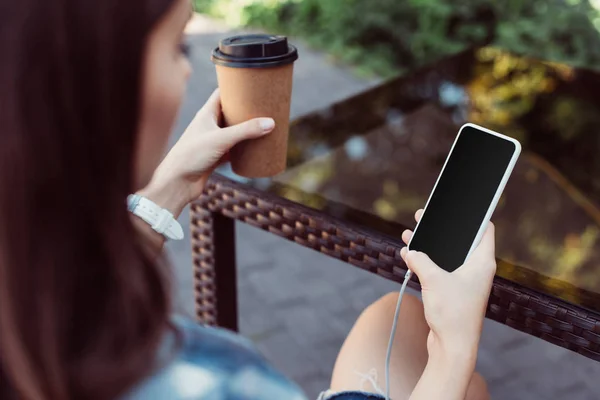 Femme utilisant un smartphone avec écran blanc à la table et tenant le café dans une tasse en papier — Photo de stock