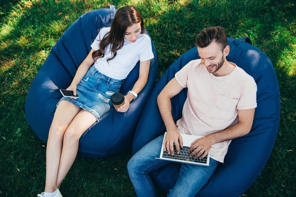 High angle view of colleagues taking part in webinar with laptop and sitting on bean bag chairs in park — Stock Photo