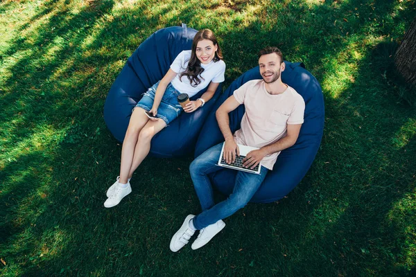 Hochwinkelaufnahme von Kollegen, die an einem Webinar auf Sitzsäcken im Park teilnehmen und in die Kamera schauen — Stockfoto