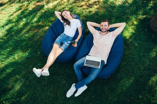 High angle view of friends lying on bean bag chairs in park and looking at camera — Stock Photo