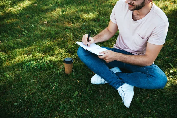 Image recadrée de l'homme prenant des notes sur l'herbe verte dans le parc — Photo de stock