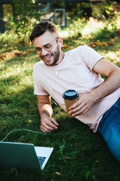 Happy handsome man taking part in webinar and lying on grass in park — Stock Photo