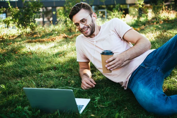 Fröhlicher gutaussehender Mann, der an Webinar teilnimmt und im Park auf Gras liegt — Stockfoto