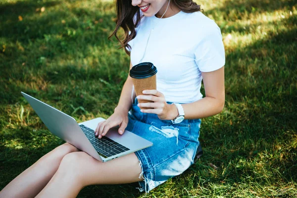 Image recadrée de fille prenant part à un webinaire avec ordinateur portable dans le parc et tenant café pour aller — Photo de stock